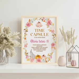 K&ouml;nnte beinhalten: Ein rechteckiges Schild in einem hellen Holzrahmen mit einem Blumenkranz aus rosa Rosen und K&uuml;rbissen. Der Text lautet: TIME CAPSULE TO BE OPENED WHEN Olivia turns 18. PLEASE WRITE A MESSAGE FOR OLIVIA. MAKE A PREDICTION OR SHARE YOUR HOPES AND WISHES.