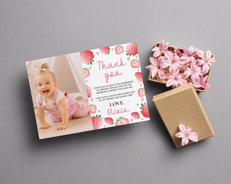 May include: A rectangular thank you card featuring a photograph of a baby in pink overalls, decorated with watercolor strawberries and hearts. The text reads: Thank you, thank you so much for celebrating my birthday with me and for the wonderful present you gave me! I had such a good time playing with all my friends and eating cake! Love, Olivia.