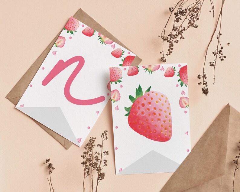 Puede incluir: Dos tarjetas de felicitaci&oacute;n blancas con ilustraciones de fresas y una letra N rosa. Una tarjeta presenta una fresa grande en acuarela, mientras que la otra muestra una letra N rosa grande. Ambas tarjetas est&aacute;n decoradas con fresas peque&ntilde;as.