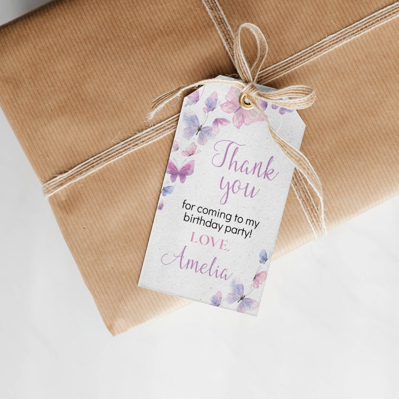 May include: A rectangular white gift tag with a gold eyelet and a natural jute twine bow. The tag features watercolor-style purple and pink butterflies and the text: Thank you for coming to my birthday party! LOVE, Amelia.