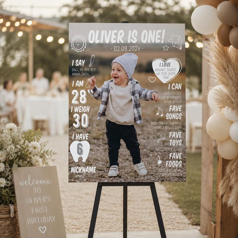 May include: A rectangular milestone birthday sign featuring a photo of a toddler in a grey beanie and plaid shirt. The text reads OLIVER IS ONE, 02.08.202x, I SAY BALL, I AM 28 INCHES, I WEIGH 30 POUNDS, I HAVE 6 TEETH, I LOVE MOMMY, DADDY, MY DOG, BATH TIME.