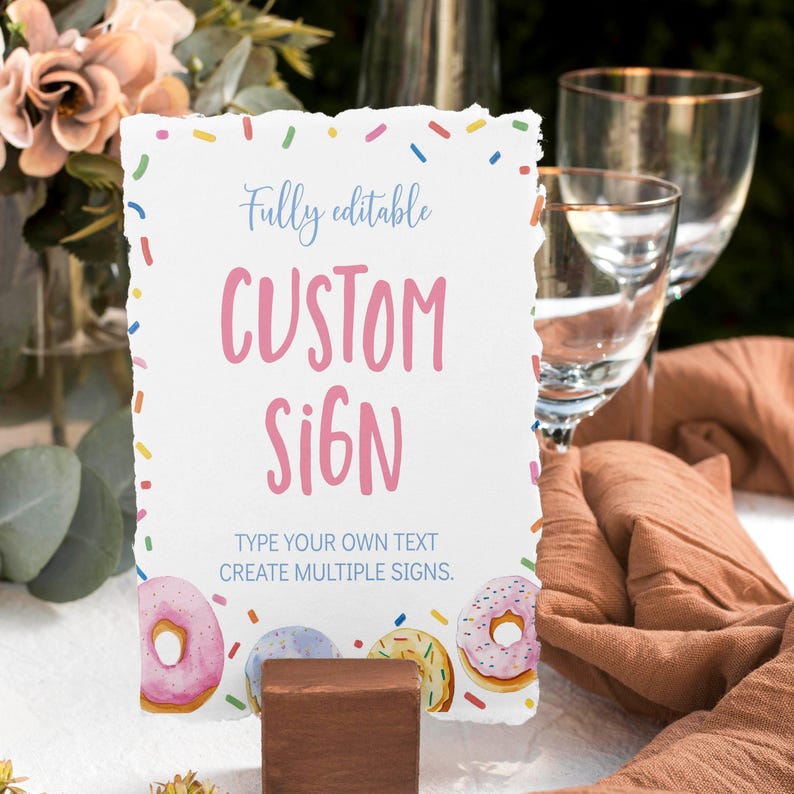 K&ouml;nnte beinhalten: Ein rechteckiges wei&szlig;es Schild mit gerissenen Kanten, einem bunten Streuselrand und Donut-Illustrationen am unteren Rand. Der Text lautet Fully editable CUSTOM SIGN TYPE YOUR OWN TEXT CREATE MULTIPLE SIGNS. Das Schild steht in einem braunen Holzblock.