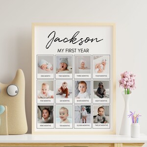 Op de afbeelding: Een rechthoekige houten lijst met een witte poster getiteld Jackson MY FIRST YEAR. De poster bevat twaalf individuele vierkante foto's van een baby, elk gelabeld met een maand van &eacute;&eacute;n tot twaalf in zwarte tekst op een witte achtergrond.
