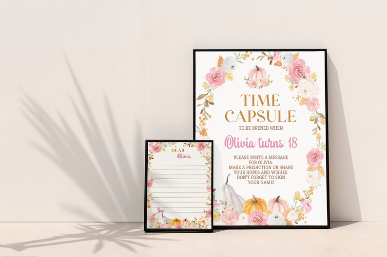 K&ouml;nnte beinhalten: Ein gro&szlig;es und ein kleines gerahmtes Schild mit einem Blumen- und K&uuml;rbiskranz-Design. Das gro&szlig;e Schild tr&auml;gt die Aufschrift: TIME CAPSULE TO BE OPENED WHEN Olivia turns 18. PLEASE WRITE A MESSAGE FOR OLIVIA. MAKE A PREDICTION OR SHARE YOUR HOPES.