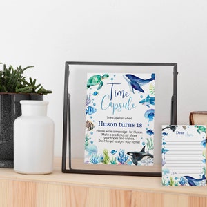 Pu&ograve; includere: Un cartello rettangolare in una cornice nera e un biglietto a righe abbinato con illustrazioni ad acquerello di creature marine tra cui una balena, una tartaruga marina, uno squalo e una medusa. Il testo recita Time Capsule, To be opened when Huson turns 18.