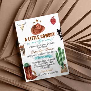 May include: A white baby shower invitation card featuring watercolor illustrations of a brown cowboy hat, a cow skull, a red bandana, a cactus, and brown leather boots. The text reads A LITTLE COWBOY is on the way! JOIN US FOR A BABY SHOWER HONORING Emily Mace SATURDAY FEBRUARY 12 AT 2PM CACTUS PARK 123 MAIN STREET SUNSHINE HILL LAS VEGAS 1236 RSVP EMILY BY FEB 08 AT 123.456.789 Registered AT TARGET & AMAZON.