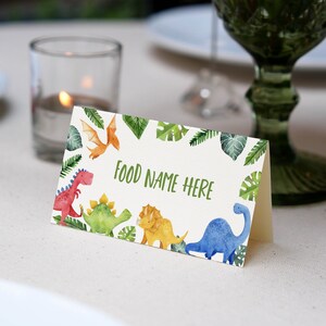 May include: A white card with a green border of leaves and dinosaurs. The text "FOOD NAME HERE" is printed in green on the card.