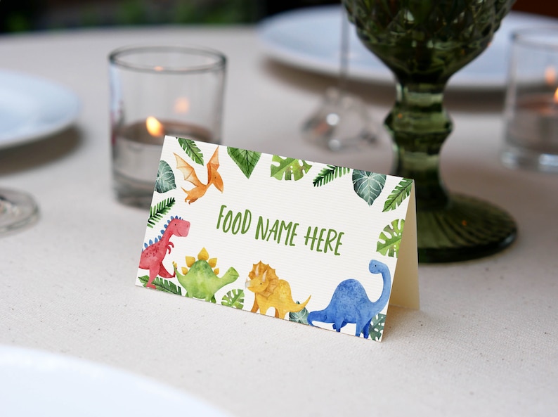May include: A white card with a green border of leaves and dinosaurs. The text "FOOD NAME HERE" is printed in green on the card.