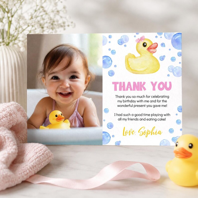 May include: A rectangular thank you card featuring a photo of a smiling child holding a yellow rubber duck. The right side displays a watercolor yellow rubber duck with a pink bow, blue bubbles, and the text: THANK YOU, Thank you so much for celebrating my birthday with me and for the wonderful present you gave me! I had such a good time playing with all my friends and eating cake! Love, Sophia.