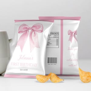 May include: Two white snack bags with pink trim featuring a large pink bow graphic. The front text reads Juliana's FIRST BIRTHDAY 25.11.202X. The back includes a nutrition facts label, a barcode, a smaller pink bow, and Thank you for celebrating with me!