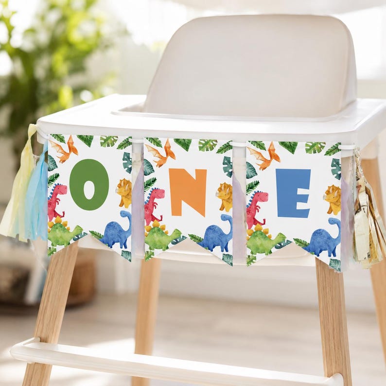K&ouml;nnte beinhalten: Ein Hochstuhl-Banner mit drei wei&szlig;en Wimpeln, die mit Aquarell-Illustrationen von Dinosauriern und tropischen Bl&auml;ttern verziert sind. Die Buchstaben O, N und E sind in gro&szlig;en gr&uuml;nen, orangen und blauen Farben gedruckt. Mit dekorativen Quasten.