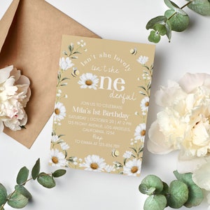 May include: A tan birthday invitation card featuring white daisy illustrations, small yellow bees, and text that reads: Isn't she lovely, isn't she one-derful, Join us to celebrate Mila's 1st Birthday, Saturday, October 20, at 2 PM, 123 Peony Avenue, Los Angeles, California, 1234, RSVP to Emma at 123.456.789.