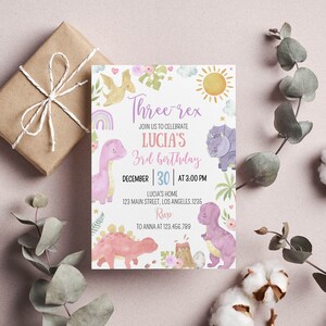 May include: A rectangular birthday invitation card featuring watercolor illustrations of dinosaurs, a sun, a rainbow, and flowers. The text reads: Three-rex, JOIN US TO CELEBRATE LUCIA'S 3rd birthday, DECEMBER 30 AT 3:00 PM, LUCIA'S HOME, 123 MAIN STREET, LOS ANGELES.1235, RSVP TO ANNA AT 123.456.789.