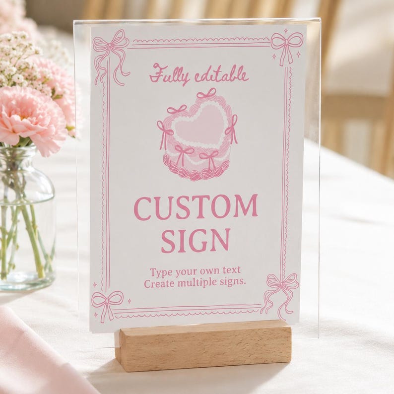 Peut inclure: Un porte-affiche en acrylique transparent avec une base en bois pr&eacute;sentant une carte blanche avec du texte et des illustrations roses. La carte affiche le texte Fully editable, CUSTOM SIGN, et Type your own text Create multiple signs.