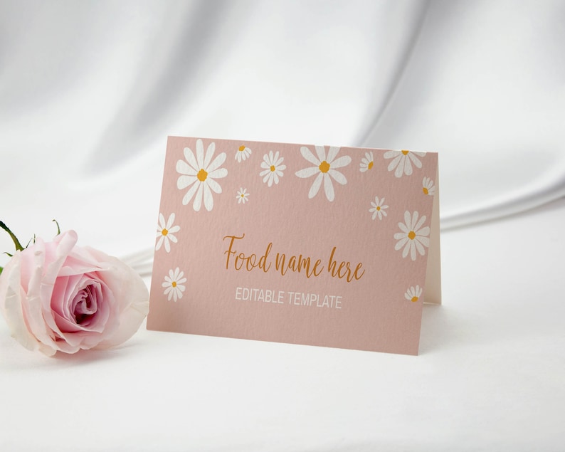 Op de afbeelding: Een gevouwen rechthoekige kaart met een oudroze achtergrond en witte madeliefjesillustraties met gele harten. De tekst luidt Food name here in goudkleurig schrift en EDITABLE TEMPLATE in witte hoofdletters. Een lichtroze roos staat ernaast.