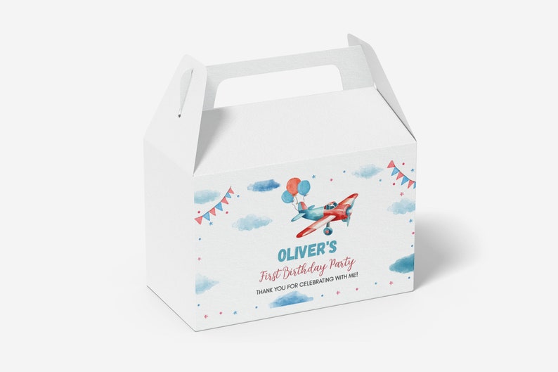 May include: A white cardboard gable box featuring a watercolor illustration of a red and blue airplane with balloons, clouds, and bunting. The text reads: OLIVER'S First Birthday Party THANK YOU FOR CELEBRATING WITH ME! The box has a top handle.