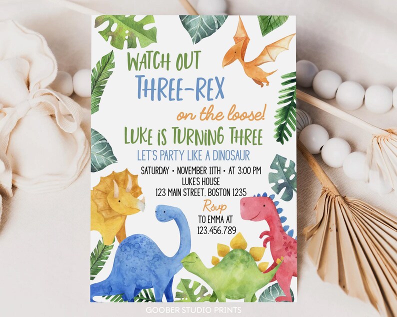 May include: A birthday party invitation with a dinosaur theme. The invitation reads "Watch Out Three-Rex on the loose! Luke is turning three." Colorful watercolor illustrations of dinosaurs and tropical leaves surround the text. The invitation includes party details.