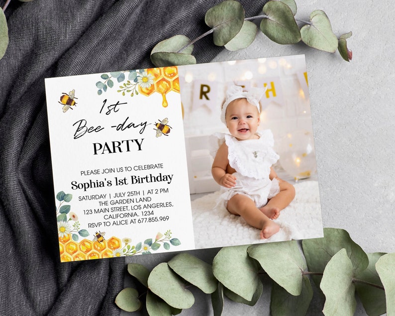 May include: A white invitation card with a bee theme for a 1st birthday party. The card features a photo of a baby girl, a honeycomb design, and the text "1st Bee-day Party". The invitation includes the party details: "Sophia's 1st Birthday", "Saturday | July 25th | At 2 PM", "The Garden Land", "123 Main Street, Los Angeles, California. 1234", "RSVP to Alice at 677.855.969".