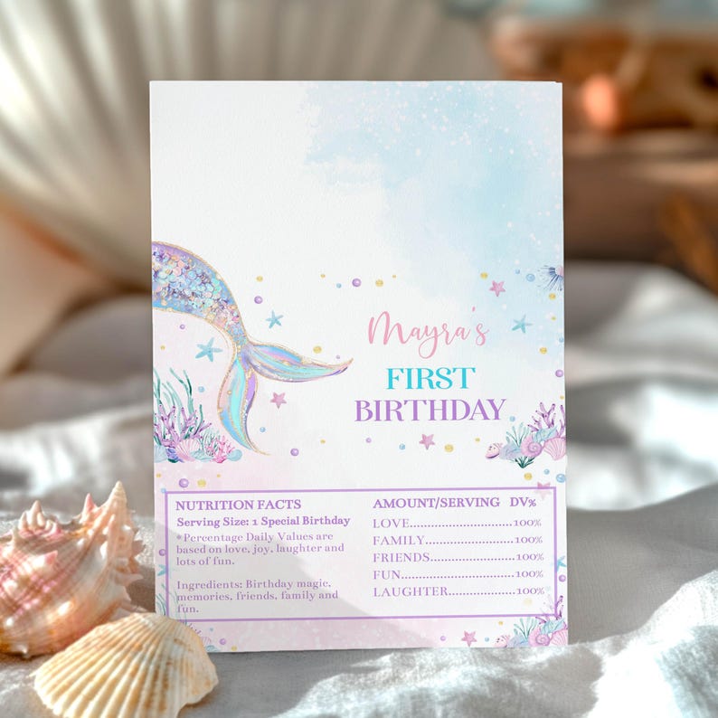 Op de afbeelding: Een rechthoekige verjaardagsuitnodiging met een pastelkleurige aquarelachtergrond, een zeemeerminstaart, schelpen en koraal. De tekst luidt Mayra's FIRST BIRTHDAY, gevolgd door een voedingswaardelabel met liefde, familie, vrienden, plezier en gelach.