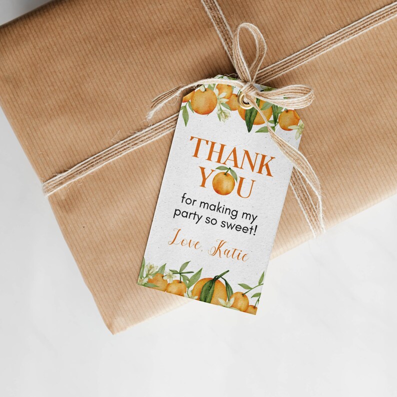 Pu&ograve; includere: Un'etichetta regalo rettangolare bianca con un motivo ad acquerello di arance e foglie verdi, con il testo arancione THANK YOU for making my party so sweet! Love, Katie. L'etichetta &egrave; fissata con un fiocco di spago beige a un pacchetto.