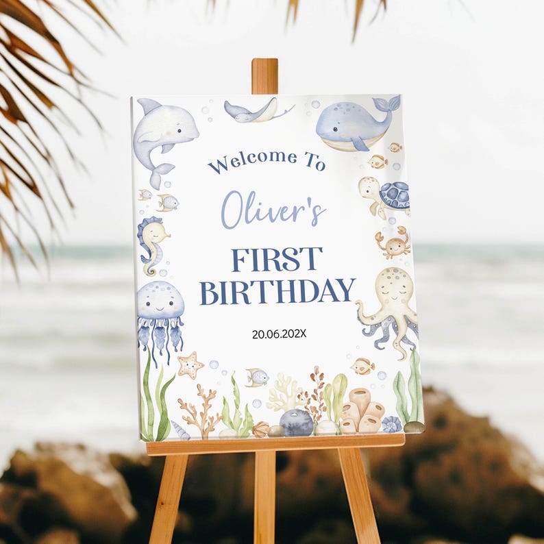 May include: A rectangular sign on a wooden easel featuring watercolour illustrations of sea creatures including a dolphin, whale, turtle, octopus, and jellyfish. The text reads Welcome To Oliver's FIRST BIRTHDAY with the date 20.06.202X below.