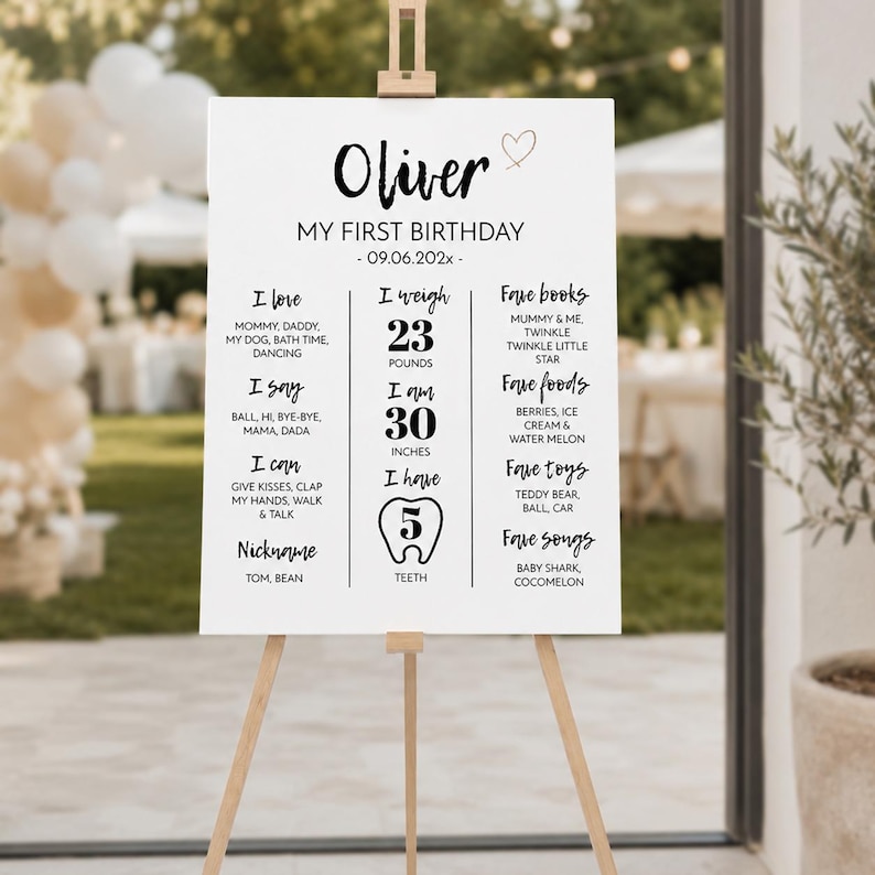 May include: A white rectangular birthday milestone sign on a wooden easel. The text reads Oliver, My First Birthday, 09.06.202x, and lists personal details including 23 pounds, 30 inches, and 5 teeth, alongside favorite books, foods, toys, and songs.