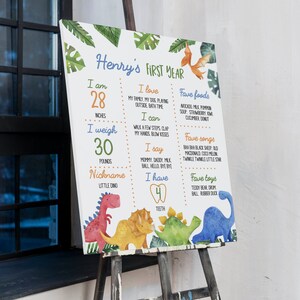 May include: A rectangular milestone board titled Henry's First Year featuring watercolor dinosaur illustrations and green leaves. It lists stats including 28 inches, 30 pounds, 4 teeth, favorite foods, songs, and toys in colorful text on a white background.