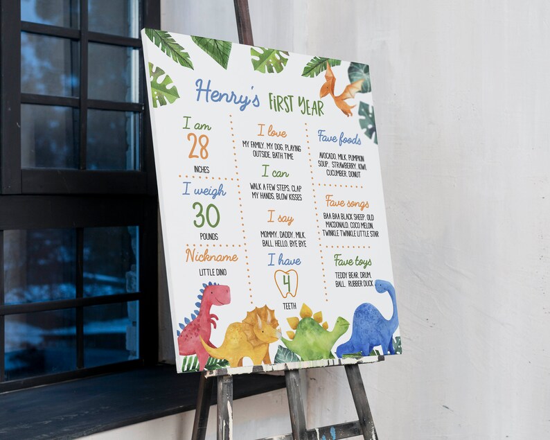 May include: A rectangular milestone board titled Henry's First Year featuring watercolor dinosaur illustrations and green leaves. It lists stats including 28 inches, 30 pounds, 4 teeth, favorite foods, songs, and toys in colorful text on a white background.