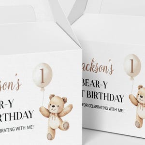 May include: Two white cardboard gable boxes featuring a printed illustration of a light brown teddy bear holding a beige balloon with the number one. The text reads Jackson's BEAR-Y FIRST BIRTHDAY THANK YOU FOR CELEBRATING WITH ME!