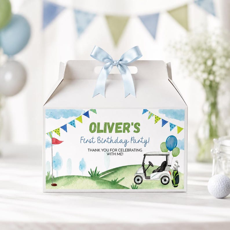 K&ouml;nnte beinhalten: Eine wei&szlig;e Schachtel mit einem hellblauen Satinband als Schleife oben. Die Vorderseite zeigt ein Golf-Motiv in Aquarelloptik mit Golfwagen, gr&uuml;nen H&uuml;geln, blauem Himmel, Wimpeln und dem Text: OLIVER'S First Birthday Party! THANK YOU FOR CELEBRATING WITH ME!