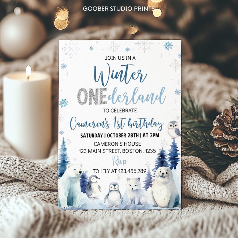 May include: A rectangular invitation card titled Winter ONEderland for Cameron's 1st birthday. The design features blue snowflakes, a polar bear, two penguins, a fox, a seal, and an owl amidst blue pine trees. Text includes date, time, and address.