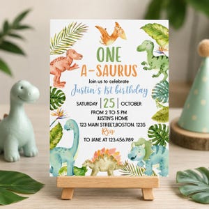 Op de afbeelding: Een rechthoekige verjaardagsuitnodigingskaart met aquarelillustraties van verschillende dinosaurussen en tropische bladeren. De tekst luidt: ONE A-SAURUS, Join us to celebrate Justin's 1st birthday, Saturday 25 October, 2 to 5 PM, Justin's home, 123 Main Street, Boston. 1235, RSVP to Jane at 123.456.789.