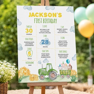 May include: A white first birthday milestone sign for Jackson featuring yellow and green text, blue clouds, and a green tractor pulling a trailer with cartoon animals. It lists weight as 30 pounds, height as 28 inches, and various personal facts.