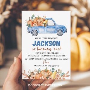 May include: A rectangular birthday invitation card featuring a blue pickup truck carrying pumpkins and the text: OUR LITTLE PUMPKIN JACKSON is turning one! JOIN US TO CELEBRATE SATURDAY | OCTOBER 10th | AT 2 PM. 123 MAIN STREET, LOS ANGELES, CA. 12345 RSVP TO EMILY AT 123.456.789.