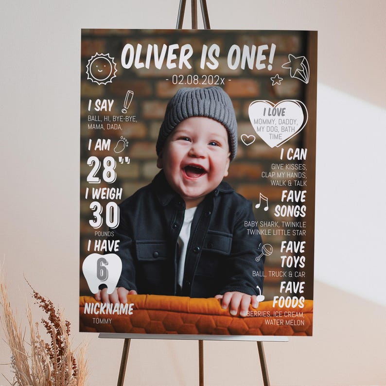 May include: A milestone birthday sign featuring a photo of a smiling child in a grey beanie and black jacket. The text includes 'OLIVER IS ONE!', birth date, weight of 30 pounds, height of 28 inches, six teeth, and lists of favorite things.