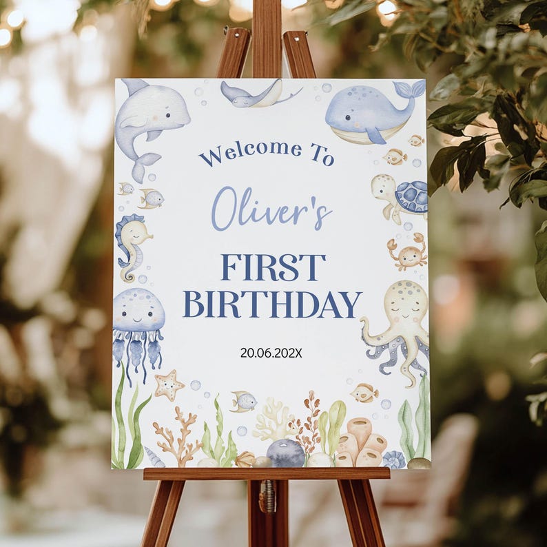 May include: A rectangular white birthday sign featuring watercolour illustrations of sea creatures including a dolphin, whale, turtle, octopus, jellyfish, and seahorse. The text reads Welcome To Oliver's FIRST BIRTHDAY and the date 20.06.202X.