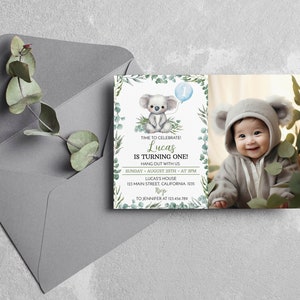 Puede incluir: Una tarjeta de invitaci&oacute;n de cumplea&ntilde;os rectangular con una ilustraci&oacute;n de koala en acuarela, un globo azul claro con el n&uacute;mero uno y hojas de eucalipto verdes. El texto dice: TIME TO CELEBRATE! Lucas IS TURNING ONE! HANG OUT WITH US.