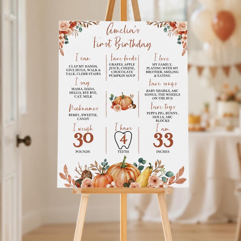 May include: A white milestone birthday sign for Amelia featuring orange pumpkin illustrations, floral accents, and text detailing milestones like 30 pounds, 4 teeth, and 33 inches, displayed on a wooden easel with a fall-themed color palette.