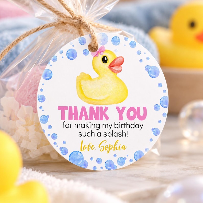 Pu&ograve; includere: Un'etichetta regalo rotonda bianca con una papera di gomma gialla con un fiocco rosa, bolle d'acqua blu e il testo THANK YOU for making my birthday such a splash! Love, Sophia. L'etichetta &egrave; attaccata a un sacchetto di plastica trasparente.