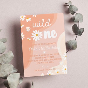 May include: A rectangular birthday invitation card in shades of peach and cream featuring white daisy illustrations. The text reads: wild one, JOIN US TO CELEBRATE Mila's 1st Birthday, SUNDAY AUGUST 10 202X FROM 2PM TO 5PM, DAISY GARDEN 123 MAIN STREET LAS VEGAS 1234, RSVP EMMA AT 123.456.789.