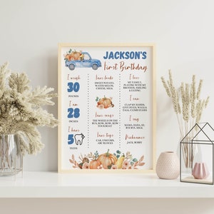 May include: A framed milestone poster for Jackson's first birthday featuring a blue truck, pumpkins, and text detailing weight of 30 pounds, height of 28 inches, 5 teeth, favorite foods, songs, toys, and personal milestones in blue and orange.