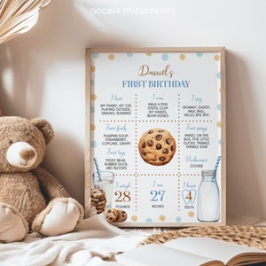 May include: A blue and yellow printable first birthday chart for a baby boy named Daniel. The chart includes information about the baby's favorite foods, toys, songs, and what he can do. It also includes his weight, height, and number of teeth. The chart is decorated with a cookie illustration.