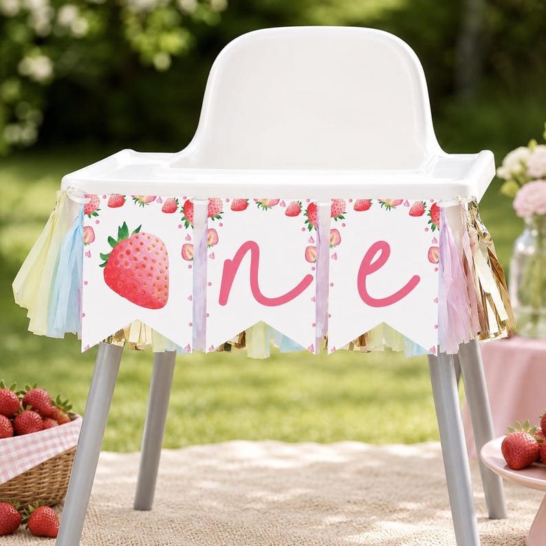 Puede incluir: Una trona blanca decorada con una pancarta que presenta ilustraciones de fresas y la palabra one en letra cursiva rosa. La pancarta est&aacute; adornada con borlas de flecos de colores pastel y met&aacute;licos dorados que cuelgan del borde.