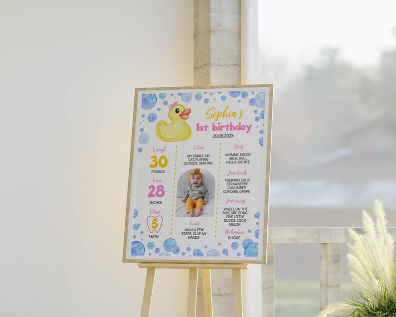 May include: A rectangular birthday milestone sign featuring a yellow rubber duck illustration, blue watercolor bubbles, and text including Sophia's 1st birthday, 20.08.202X, 30 pounds, 28 inches, 5 teeth, and a central photograph of a baby in a yellow outfit.