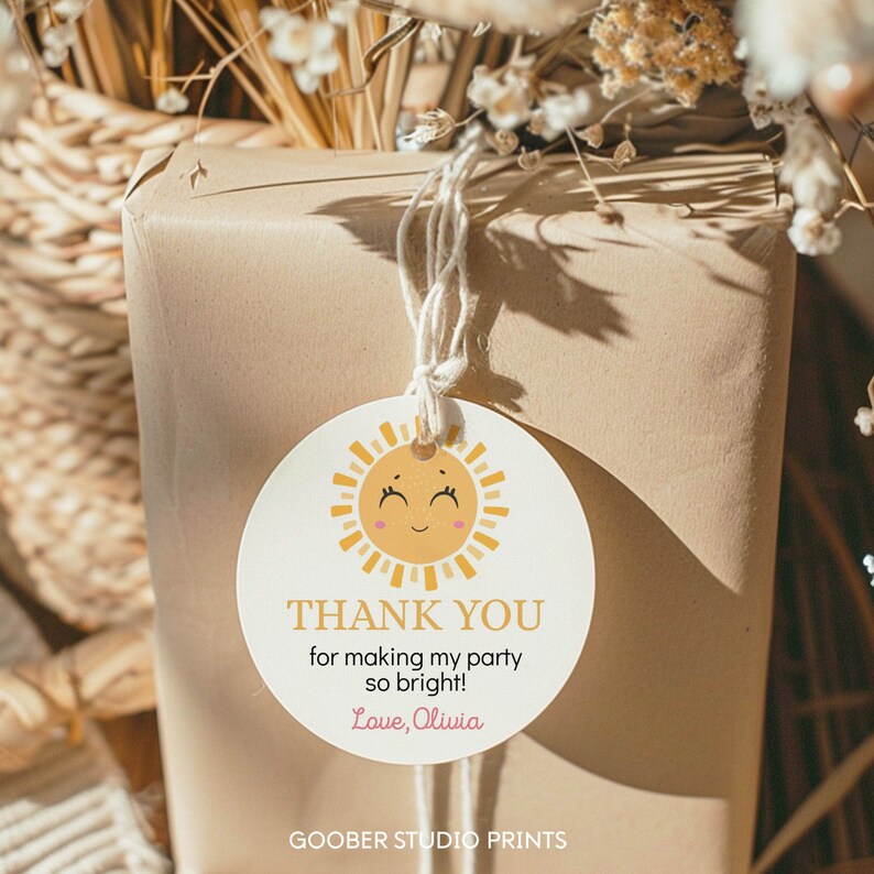 May include: A round white gift tag featuring a yellow sun illustration with a smiling face and pink cheeks. The text reads THANK YOU for making my party so bright! Love, Olivia. The tag is attached with white string to a brown paper wrapped package.