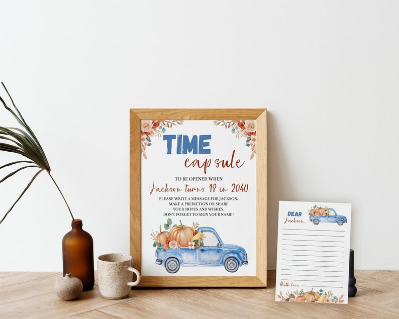 May include: A framed sign titled TIME capsule with text to be opened when Jackson turns 18 in 2040, featuring a blue truck carrying pumpkins and floral accents. Beside it is a lined card with the text Dear Jackson and a blue truck illustration.