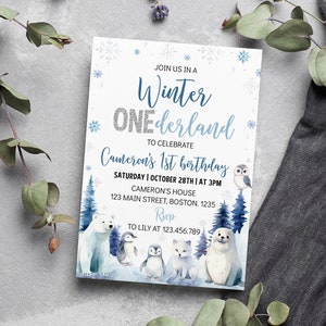 May include: A rectangular invitation card featuring a winter theme with blue and silver text reading Winter ONEderland to celebrate Cameron's 1st birthday. The design includes watercolor illustrations of a polar bear, penguins, a fox, and a seal.