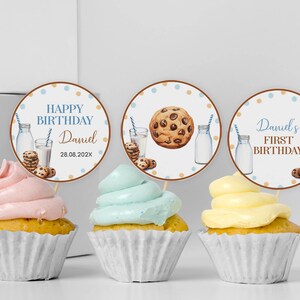 May include: Three cupcakes with pink, light blue, and yellow frosting in white paper liners, each topped with a circular card featuring illustrations of milk glasses, cookies, and text including Happy Birthday Daniel 28.08.202X and Daniel's First Birthday.