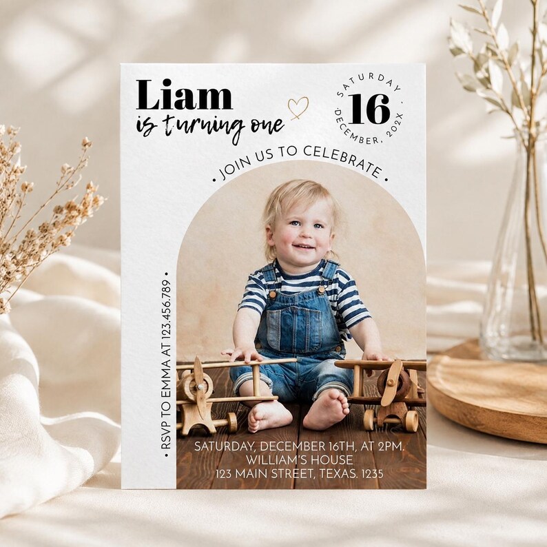 May include: A rectangular birthday invitation card featuring a photo of a child in denim overalls and a striped shirt sitting with wooden toy airplanes. The text reads Liam is turning one, Saturday December 16, 202X, Join us to celebrate, RSVP to Emma at 123.456.789, Saturday December 16th at 2pm, William's house, 123 Main Street, Texas. 1235.
