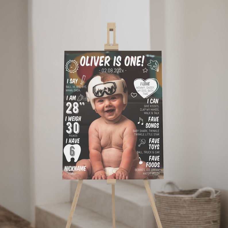 May include: A rectangular birthday milestone sign featuring a photo of a baby wearing a white medical cranial helmet. The black background includes white text detailing the baby's age, height of 28 inches, weight of 30 pounds, and favorites.